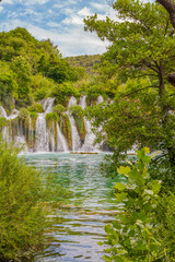 Krka National Park, Croatia, view of the Krka waterfall on a sunny day, featuring cascading water, lush greenery, wooden walkways, and a stunning natural landscape in bright Mediterranean light. © johnkruger1