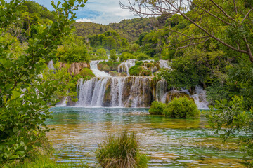Krka National Park, Croatia, view of the Krka waterfall on a sunny day, featuring cascading water, lush greenery, wooden walkways, and a stunning natural landscape in bright Mediterranean light. © johnkruger1