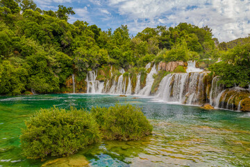 Krka National Park, Croatia, view of the Krka waterfall on a sunny day, featuring cascading water, lush greenery, wooden walkways, and a stunning natural landscape in bright Mediterranean light. © johnkruger1