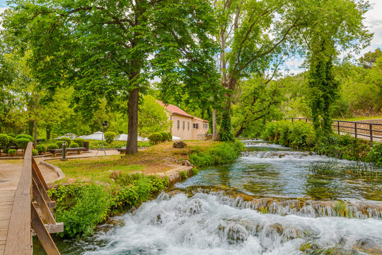 Picturesque historic watermills and a stone bridge in Krka National Park, Croatia, surrounded by lush greenery, flowing river water and beautiful natural scenery on a sunny summer day.