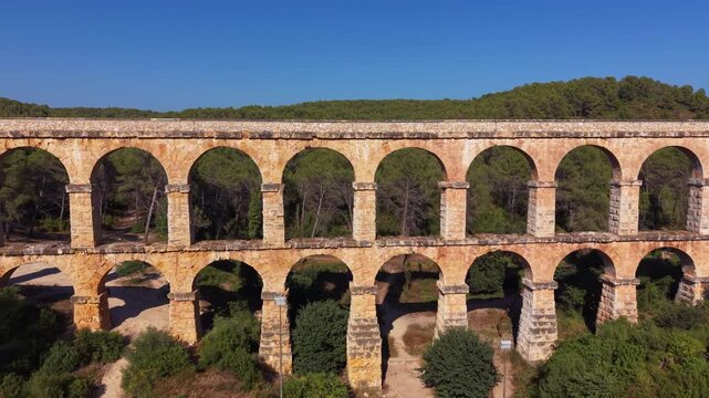 Aerial view of Pont del Diable, a UNESCO Roman aqueduct near Tarragona, Catalonia, Spain, featuring symmetrical double-tiered stone arches framing dense pine forest under clear blue sky