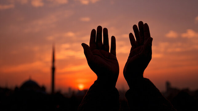 Silhouette of cupped hands raised in Islamic prayer against a beautiful sunset sky with a mosque background.