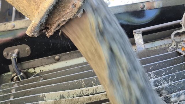 Slow motion close up of thick wet concrete mixture flowing and dropping from a metal chute into a pump machine.
