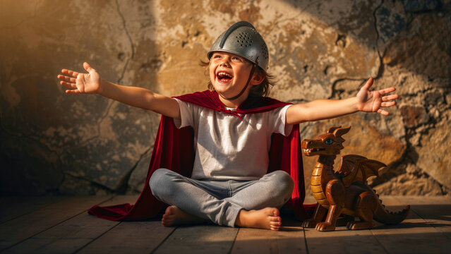 Joyful young boy wearing a knight helmet and red cape laughing with arms wide open. Child playing fantasy hero role-play with a wooden dragon toy. Childhood imagination and adventure concept.