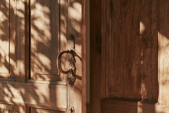 Close view of a warm wooden door with a vintage handle and keyhole, rich grain and sunlight creating a rustic country home mood full of charm and age.