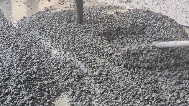 Slow motion of workers manually spreading fresh coarse gravel concrete mixture with steel rakes on a construction site.