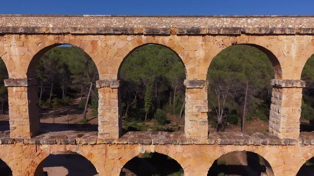Close aerial view of weathered stone arches on Pont del Diable, an ancient Roman aqueduct near Tarragona, Catalonia, Spain, with pine forest visible through the openings