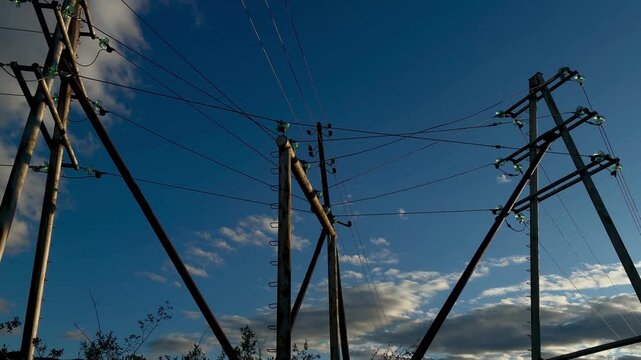 Dramatic low angle shot of high voltage electricity power lines and transmission pylons against a beautiful blue sky with clouds.