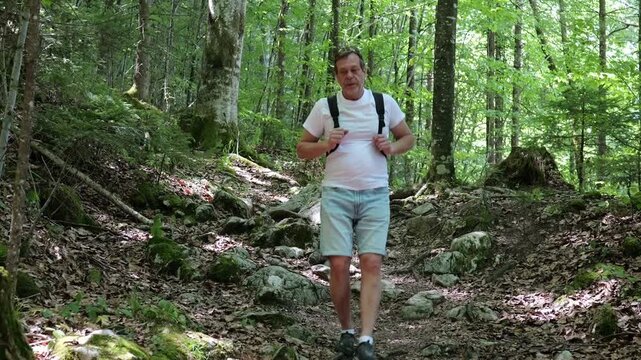 55 year old man with backpack hiking on rocky trail through green forest