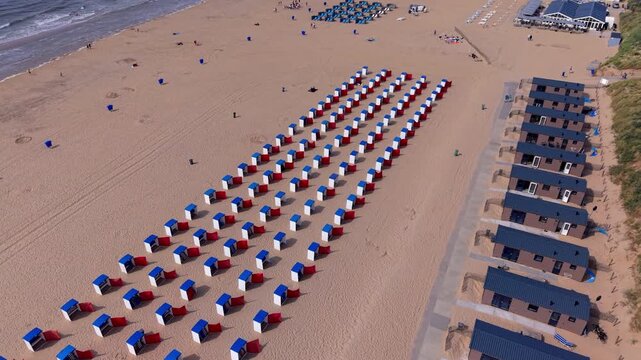 Aerial view video clip of Katwijk aan Zee beach resort, white, red, blue beach cabins, wooden holiday bungalows, sand dunes, and North Sea shoreline in South Holland, Netherlands on a sunny summer day