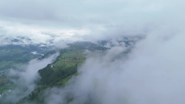 Drone flying through heavy white clouds revealing a rural farming valley and winding river below in the Himalayas