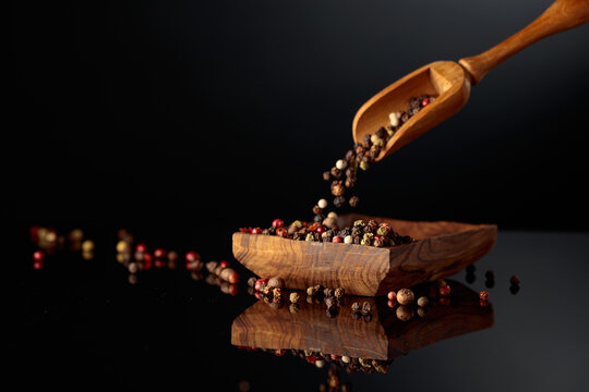 Black, red, white, and allspice peppercorns is poured in wooden dish.