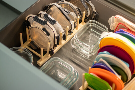 Organized kitchen drawer containing glass food storage containers with colorful lids and plastic containers neatly arranged on wooden dividers for efficient storage