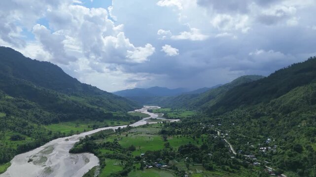 Wide aerial view of a braided muddy river flowing through a deep green valley under dark clouds