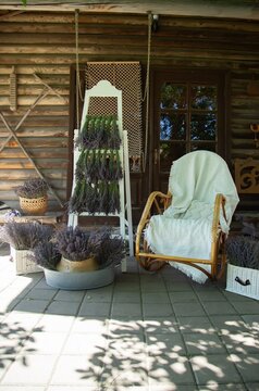  Lavender bundles dry on a white wooden rack on a rustic porch. Baskets filled with lavender surround a wicker chair, creating a serene and fragrant outdoor scene