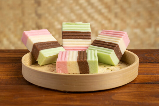 Traditional Indonesian layered sweet snack called Gethuk Trio made from mashed cassava, served on a woven bamboo tray over a wooden table.
