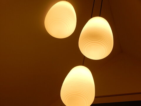 Vue en contre-plong&eacute;e de trois luminaires suspendus aux formes arrondies diffusant une lumi&egrave;re chaude, cr&eacute;ant une ambiance int&eacute;rieure douce et chaleureuse.