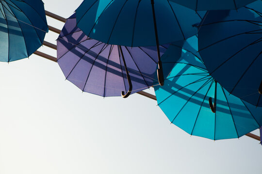 Blue and turquoise umbrellas hang against an open white sky, minimalist outdoor decoration, creative festival background.