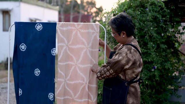 Senior tie dye small business owner inspecting finished handmade textiles outdoors, quality control, artisan skill, creative enterprise, active retirement, productive aging lifestyle.