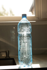 Plastic water bottle standing upright on kitchen counter with condensation amid shortage awareness © olga_sova