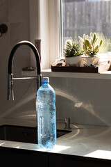 Large blue-capped plastic water bottle stands upright on sunlit kitchen counter near sink © olga_sova