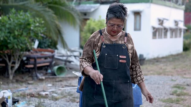 Healthy retired woman stirring steaming dye bath outdoors, handmade textile production, artisan craft skill, small business routine, independent work, productive aging lifestyle business.