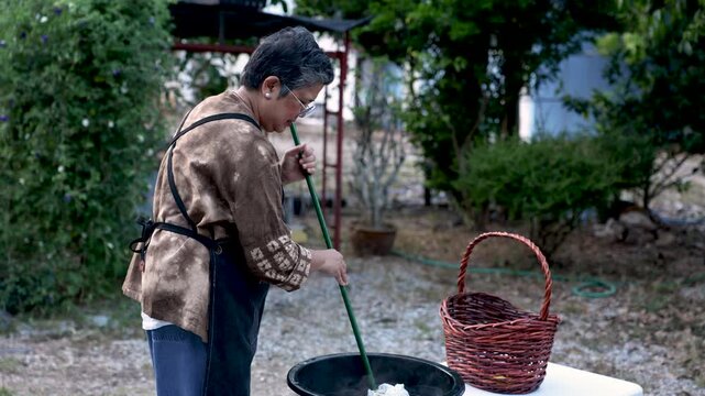 Senior craft business owner stirring tie dye fabric outdoors, skilled textile work, independent entrepreneurship, active retirement, productive aging, creative lifestyle, handmade craft.