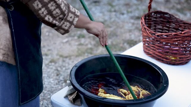 Healthy senior woman stirring fabric in natural dye bath outdoors, hands on textile craft, small business activity, active retirement, skilled work, creative lifestyle, productive aging.