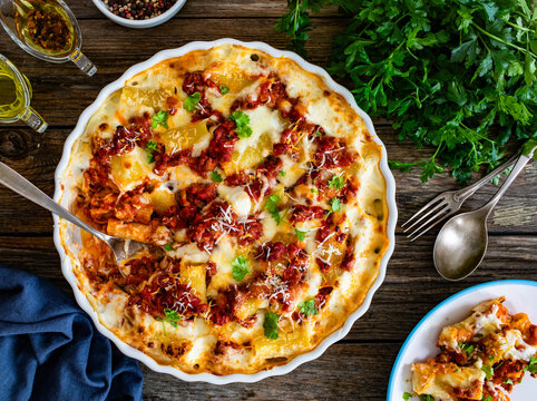Bolognese pasta casserole - baked rigatoni noodles with bolognese sauce, mozzarella cheese and b&eacute;chamel sauce on wooden table. Top view
