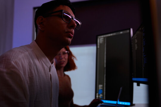 Late night software developers and programmers with glasses working intensely in dark office, analyzing generic code on vertical monitors for a tech startup innovation project.