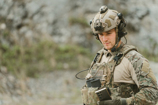 Outdoor military concept. Portrait of focused soldier wearing tactical gear looking calm with determined expression while training in rocky field environment