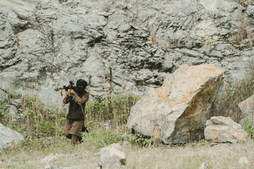 Obraz premium Outdoor military concept. Soldier with rifle focused in hostile terrain with intense expression, warrior alert during combat mission in rocky wilderness environment
