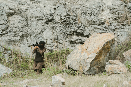 Outdoor military concept. Soldier with rifle focused in hostile terrain with intense expression, warrior alert during combat mission in rocky wilderness environment