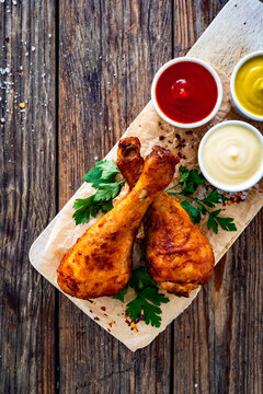 Air fryer chicken drumsticks with mayonnaise, ketchup and mustard on wooden table. Top view


