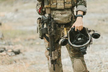 Fototapeta premium Outdoor military concept. Determined soldier standing with equipment, rifle, and helmet feeling proud and professional while training in desert field