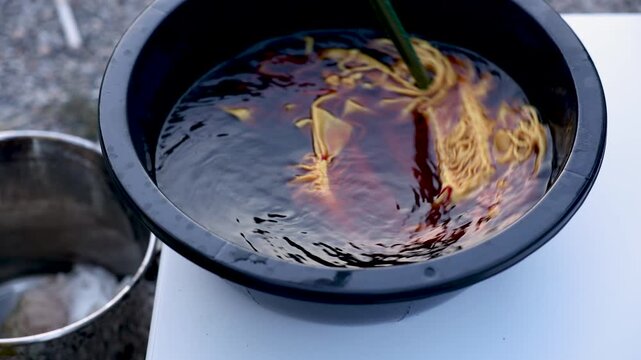 Close up dyed fabric immersed in natural dye solution outdoors, tie dye craft process, handmade textile production, artisan workshop, material treatment, creative small business work.