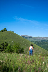 Fototapeta premium Rolling green hills under a clear blue sky with a distant hiker