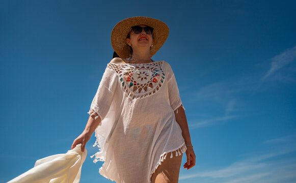 Beautiful middle-aged woman enjoying walk on sandy beach Monte Clerigo in Portugal on sunny summer day. Front view
