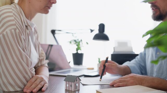 Professional real estate broker discussing the terms of a house sale or rental agreement with a customer, pointing to the contract while negotiating the deal in a modern office