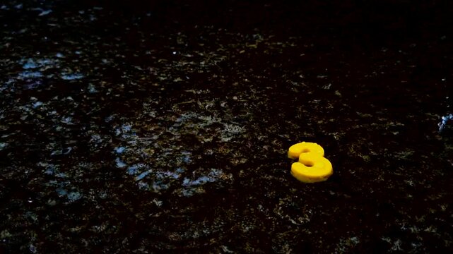 Yellow number three figurine on dark distressed surface digit weathered texture ground concrete