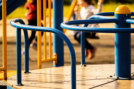 Close-up of a blue and yellow playground merry-go-round with children playing in the background