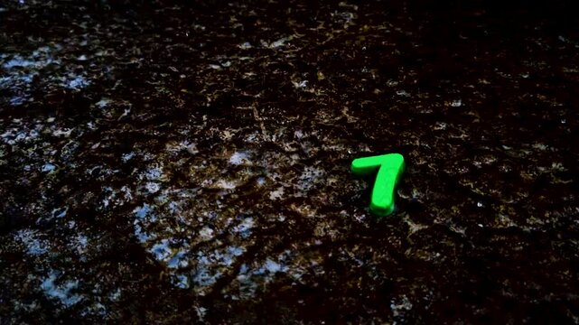 Green plastic number seven toy lying on dark wet ground in rain pavement water droplets storm