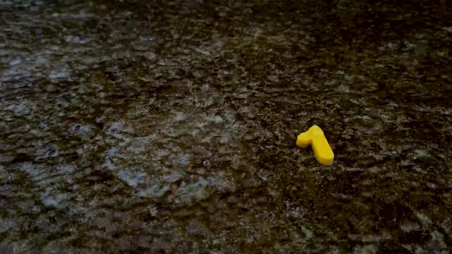 Yellow plastic number one toy on wet concrete during rain shower ground pavement water droplets