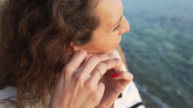 Woman jewelry earring adjusting close-up profile view of attractive female putting on accessory at sunset.