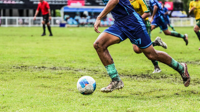 Soccer player sprinting with the ball on a muddy grass field during football match