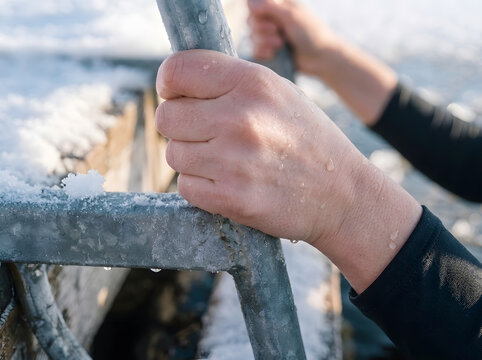 Bare Hand Holding Metal Railing in Ice and Snow Close Up | Person Gripping Freezing Metal Ladder Outdoor in Winter | Wet Hands Holding Icy Metal Bar During Winter Swimming 