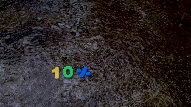 Ten percent discount sign composed of colorful plastic numbers on a wet dark pavement surface