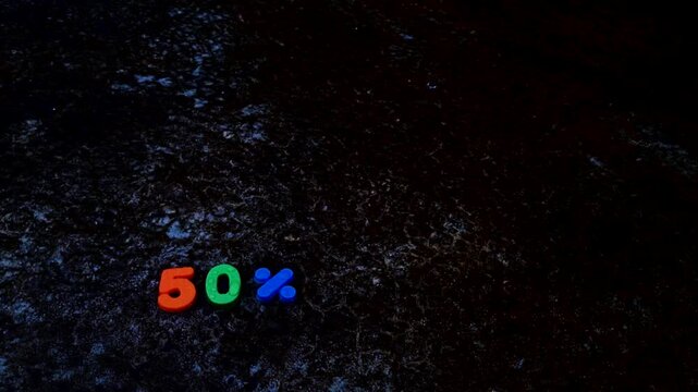 Fifty percent discount sign made of colorful plastic numbers on a dark wet texture surface
