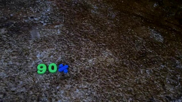 Ninety percent text sign made with green and blue plastic numbers on wet dark pavement