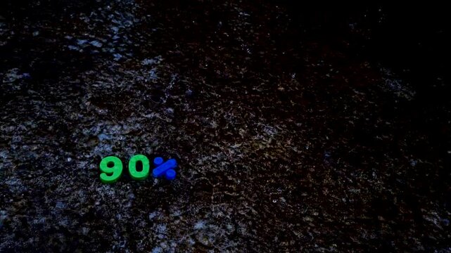 Ninety percent text sign made with green and blue plastic numbers on dark damp ground